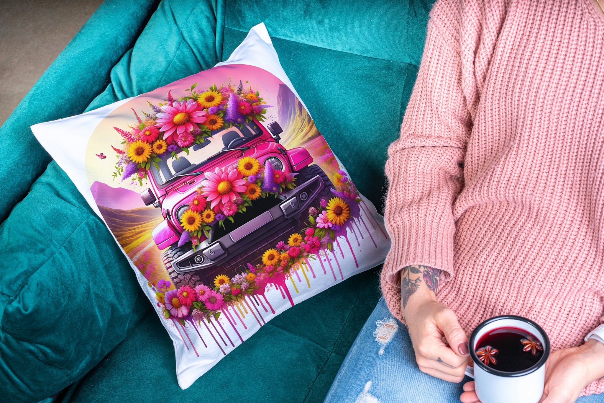 Decorative pillow with a colorful car and flowers design on a teal couch, person holding a mug.