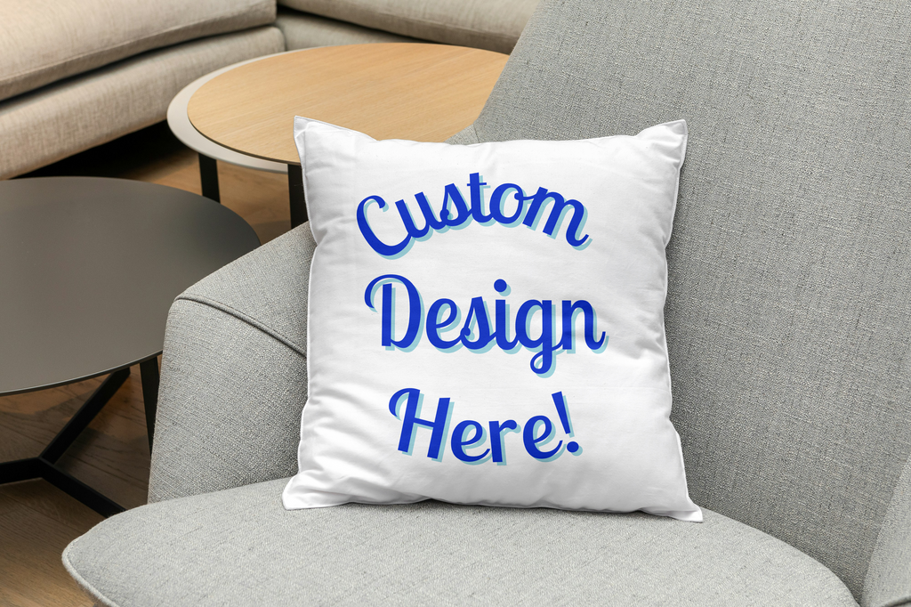 White pillow with blue text 'Custom Design Here!' on a gray couch.